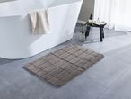 A gray bath mat on a tiled floor next to a white bathtub with a towel.