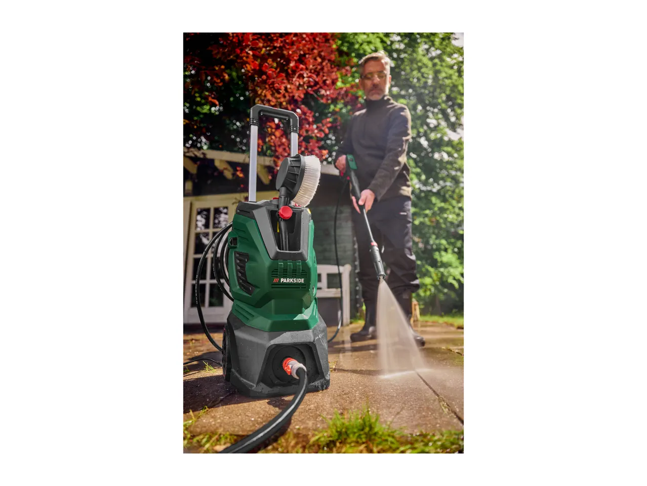 A man pressure washing a patio with a green and black pressure washer.
