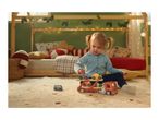 A child playing with a wooden car transporter toy on a rug in a festive bedroom.