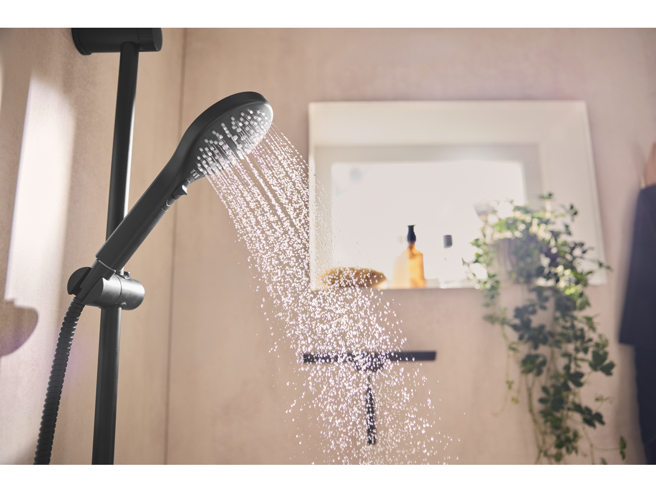 Zwarte handdouche met waterstraal in een moderne badkamer met plant en accessoires.