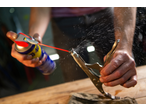 Um homem limpa uma peça de metal com spray lubrificante e alicates.