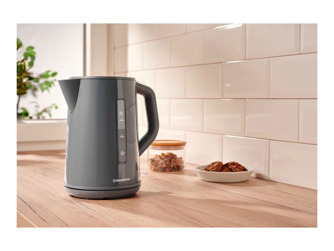 A dark grey SilverCrest electric kettle on a wooden countertop with cookies and sugar.