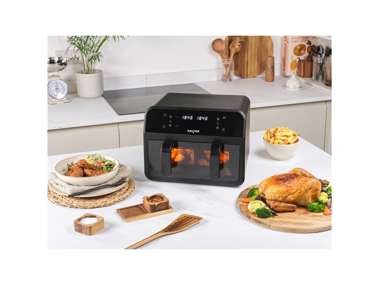 A black Salter air fryer on a kitchen counter with cooked chicken, fries, and salad.