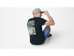 Model masculin așezat, purtând un tricou cu mâneci scurte cu imprimeu de plajă și o șapcă.