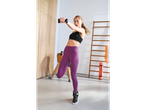 Mulher com sapatilhas desportivas Crivit, leggings roxos e sutiã desportivo preto, a levantar halteres.