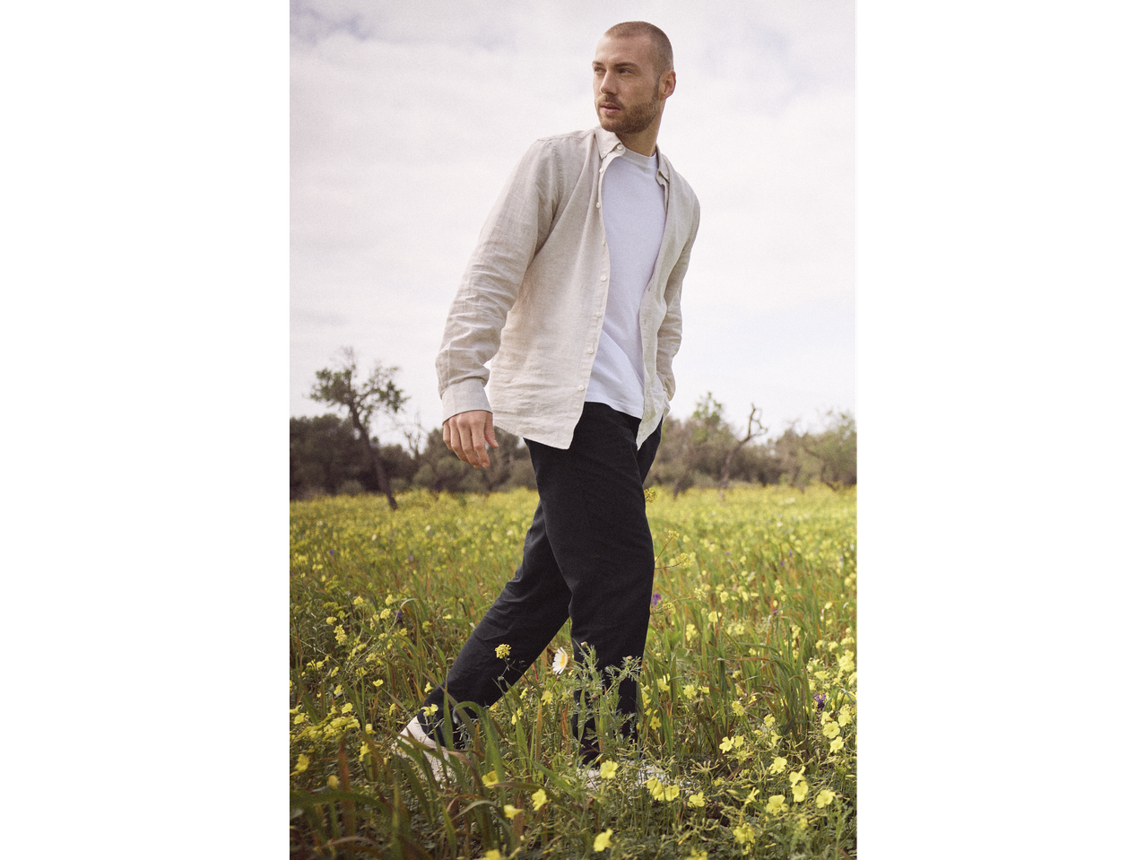 Man walking through a field of flowers wearing a linen shirt and black pants.