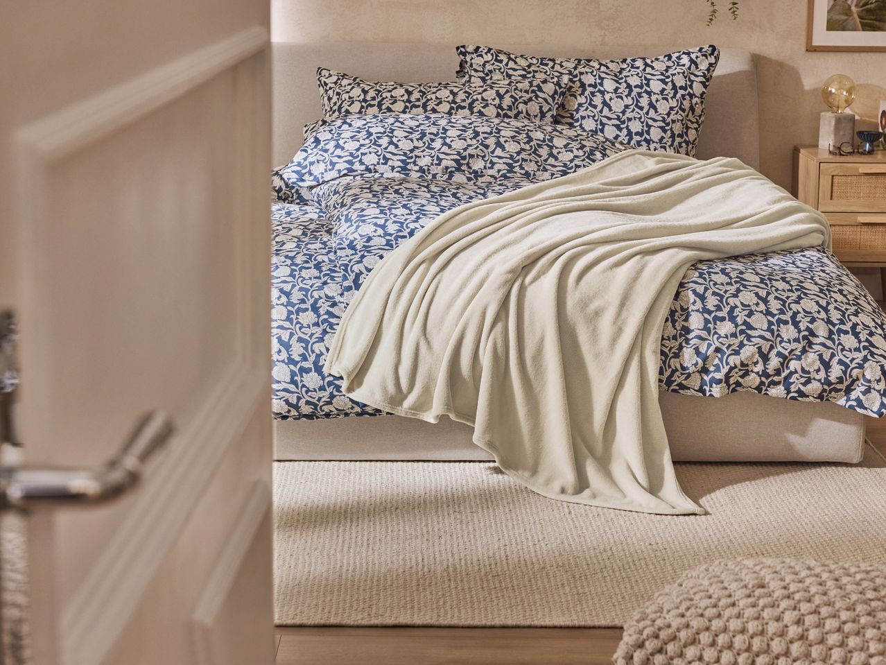 Bedroom with a bed featuring blue and white floral bedding and a cream throw blanket.