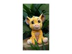 A plush toy of a lion cub sitting on a wooden stump with green foliage in the background.