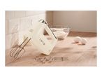Cream hand mixer with beaters and dough hooks on a wooden counter with baking ingredients.