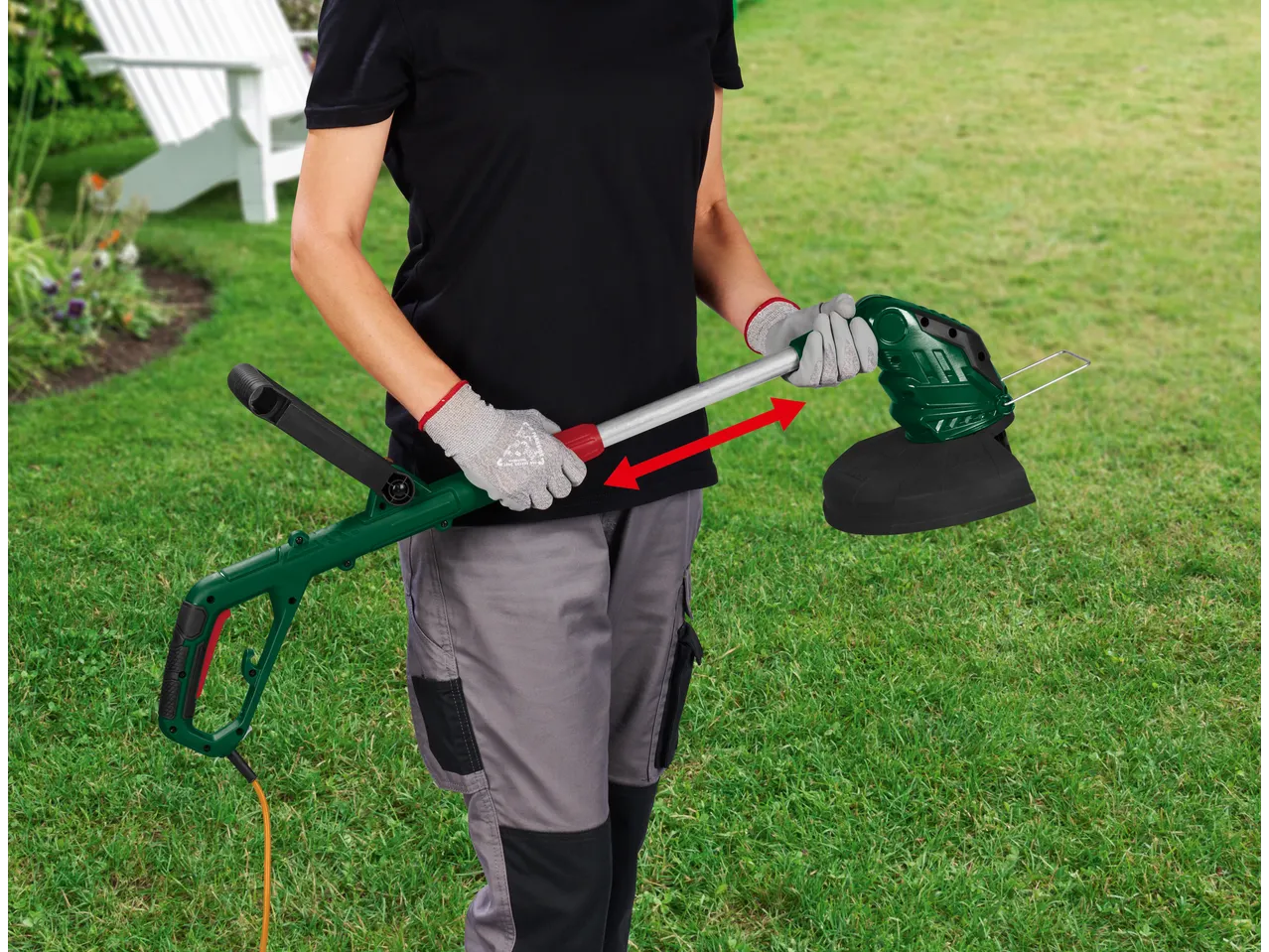 Person holding a green and black electric grass trimmer with an orange cable in a garden.