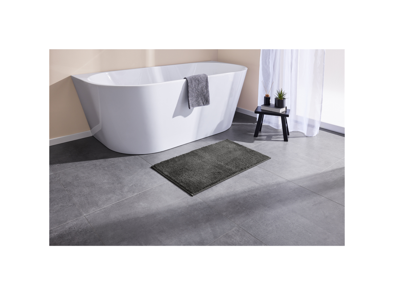 Dark gray bath mat next to a white bathtub.