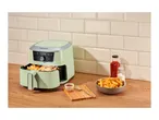 Green air fryer with fries, ketchup, and salt on a wooden counter.
