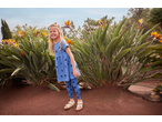 Smiling girl in a blue heart-print dress and leggings, standing among bird of paradise plants.