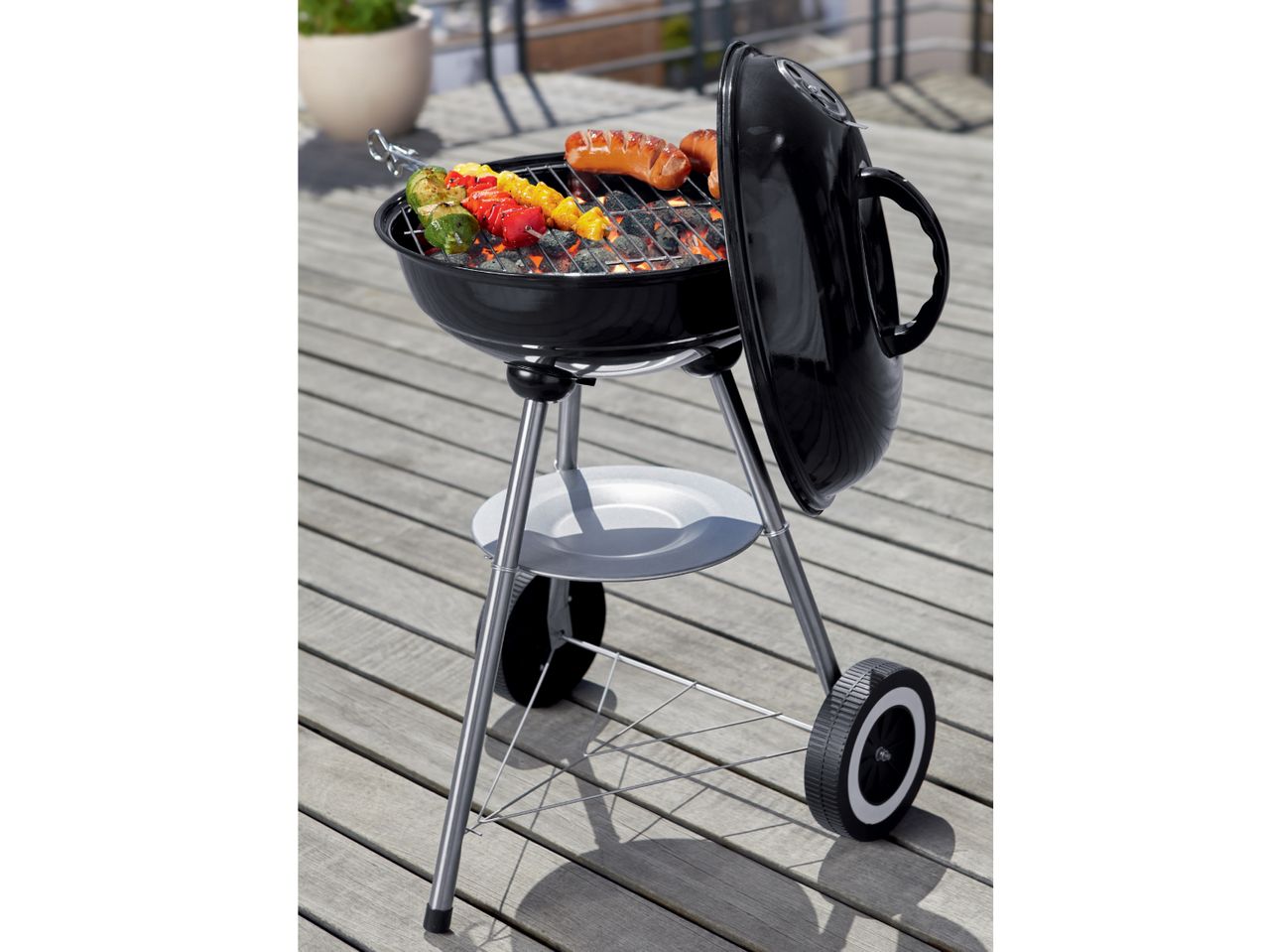 Kettle charcoal grill with sausages and vegetable skewers.