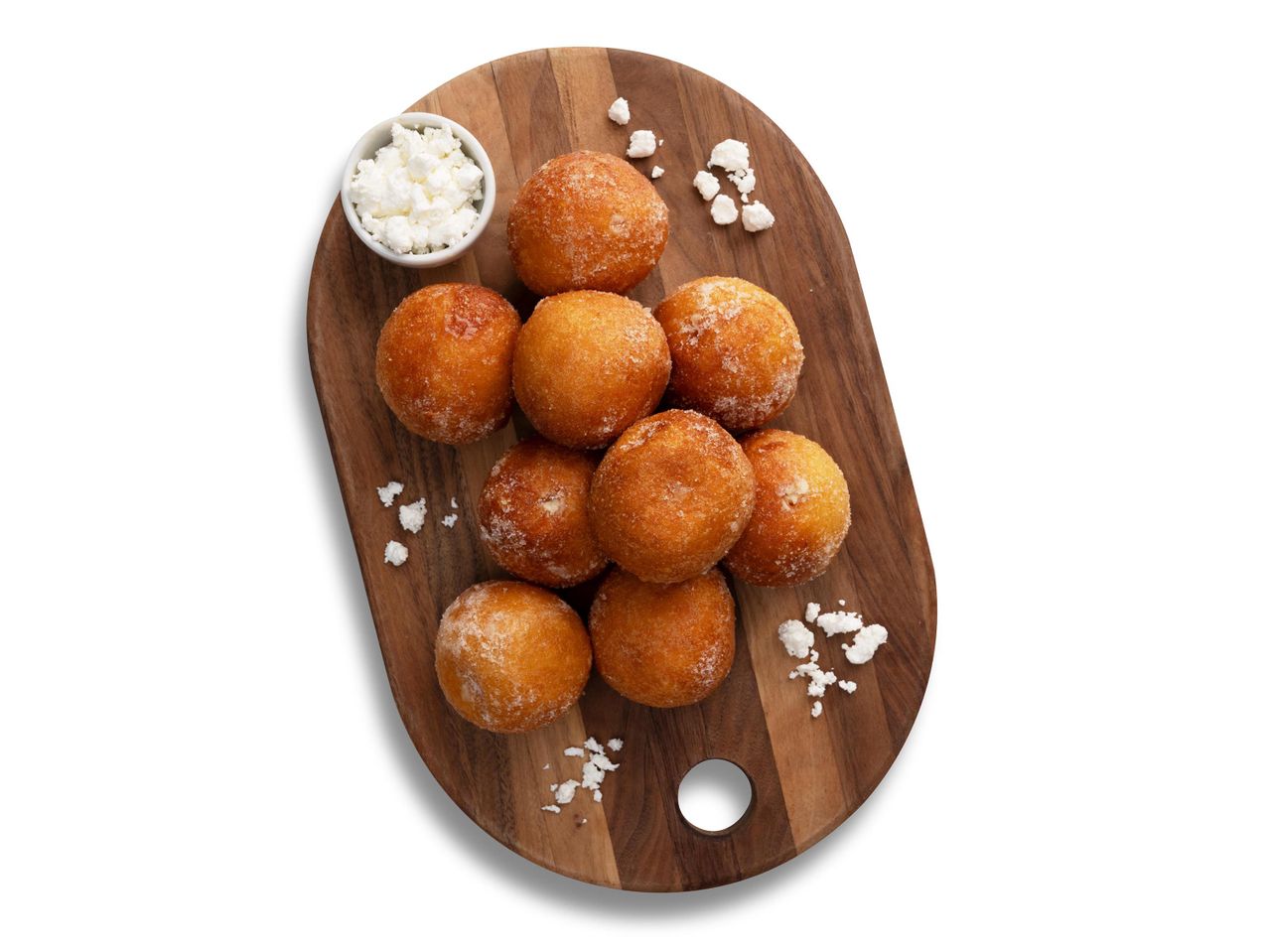 Aranybarna fánkocskák cukorral megszórva, egy tál túróval egy fa vágódeszkán.