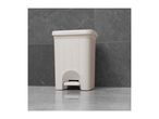 A white plastic step-on trash can sits on a gray floor.