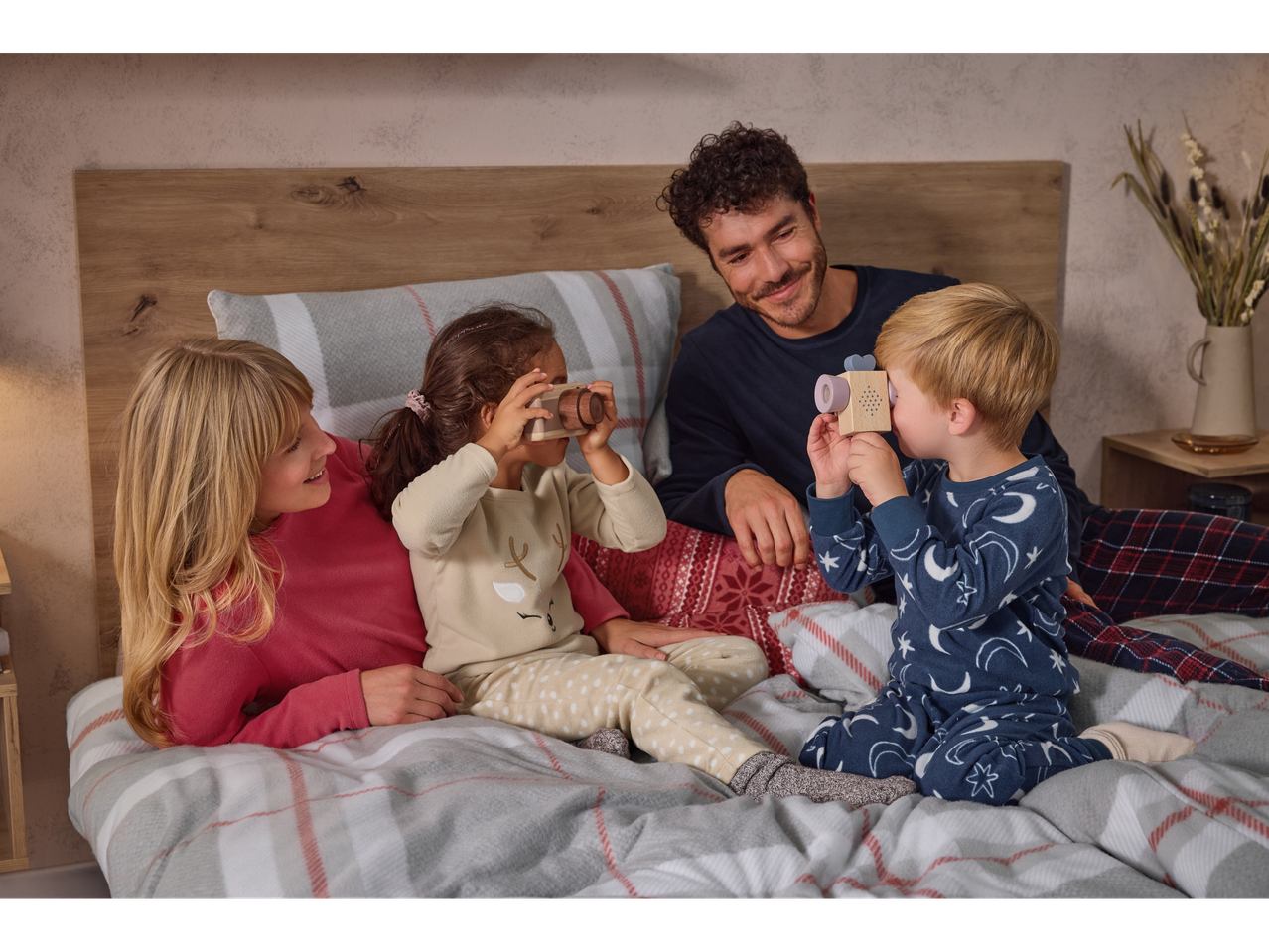 Family in fleece pajamas on a bed, children playing with toy cameras.