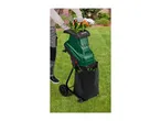 Person in work gloves feeding green garden shredder with leaves, collecting into a black bag.