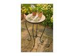 Round mosaic garden table with two potted plants on a patio, surrounded by flowers.