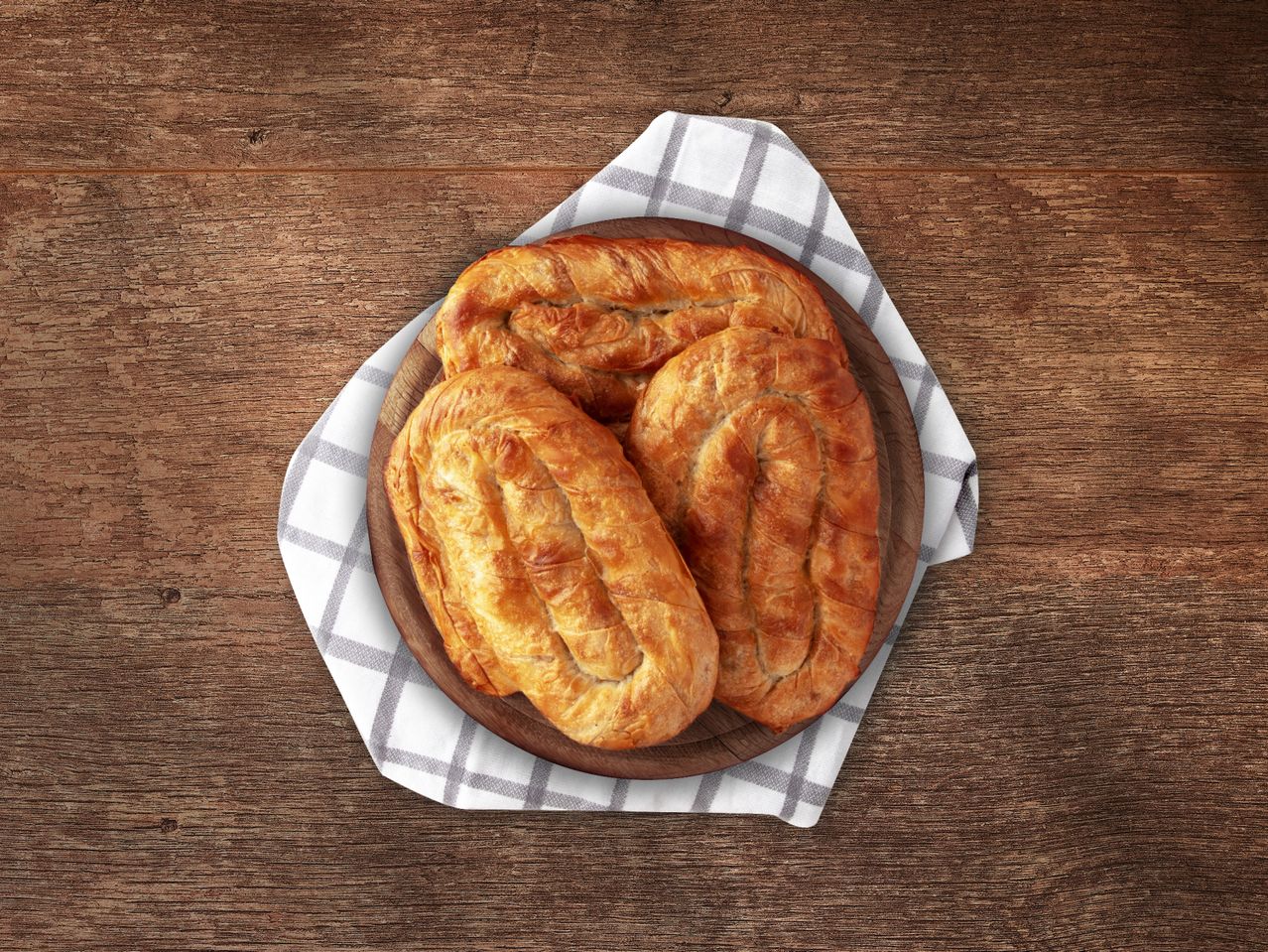 Tri zlatno-smeđa bureka na drvenoj dasci za posluživanje s kariranom krpom.