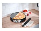 Crepe maker with a folded crepe, strawberries, and jam on a wooden counter.