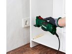 A person uses a multi-tool to sand the inside of a white cabinet, creating sawdust.