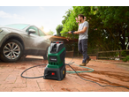 Man using a PARKSIDE® 1800W Pressure Washer to clean a dirty car on a brick patio.