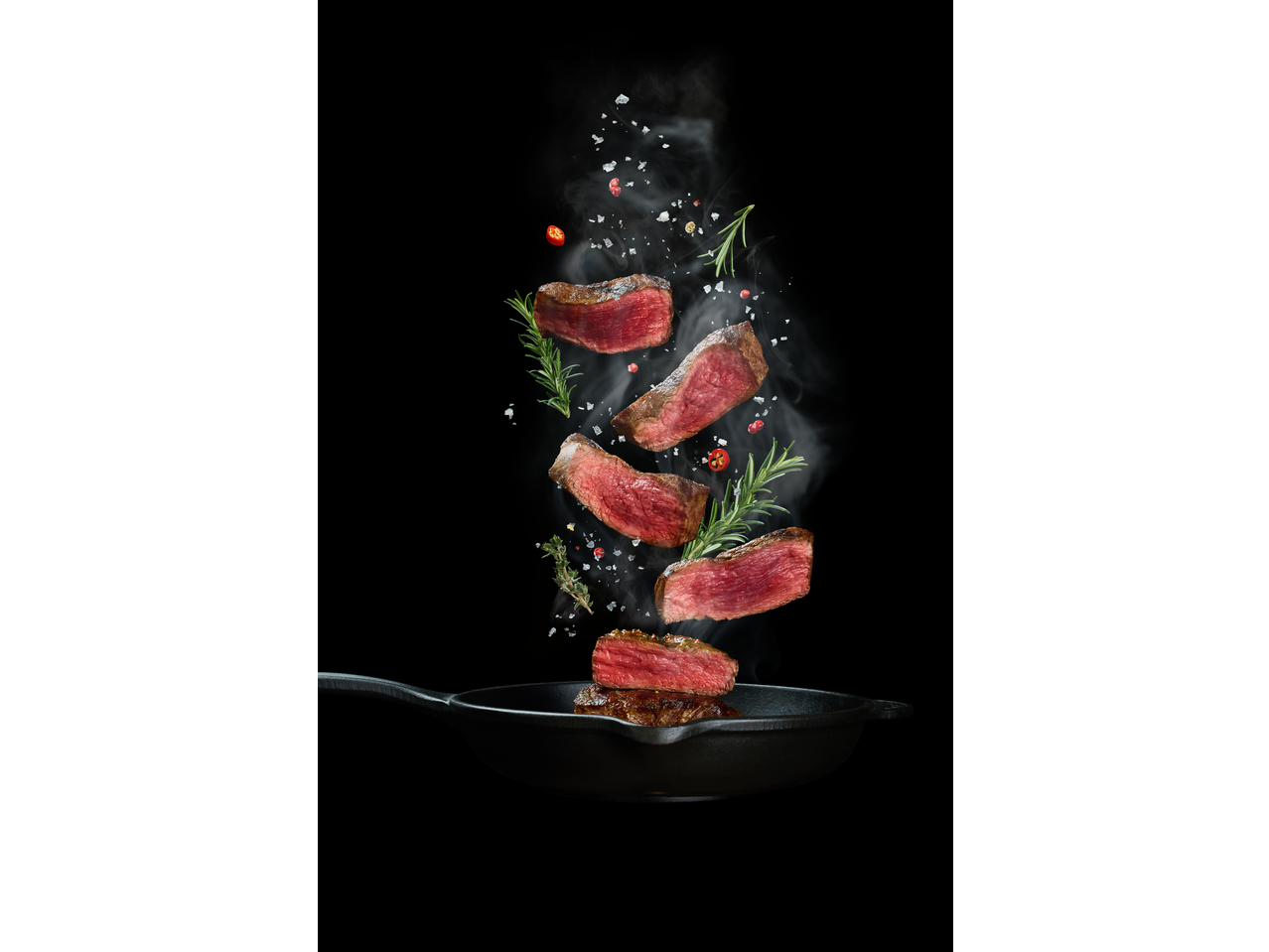 Filetes de carne grelhados com alecrim, pimenta e sal, flutuando sobre uma frigideira.