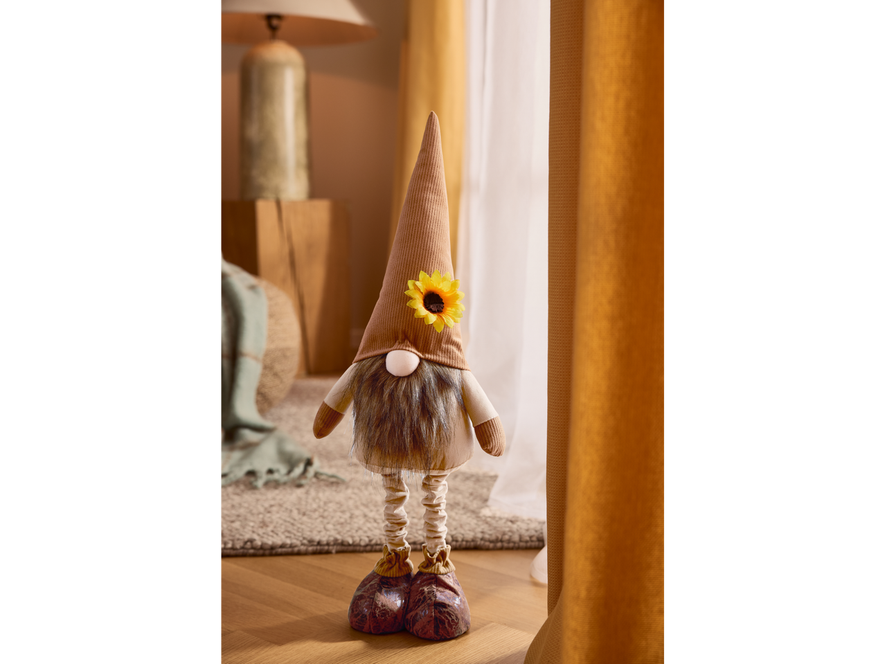 A decorative gnome with a sunflower on its hat stands on a wooden floor.