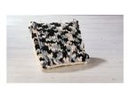 A chunky knit pillow in black, white, gray, and purple on a light wooden surface.
