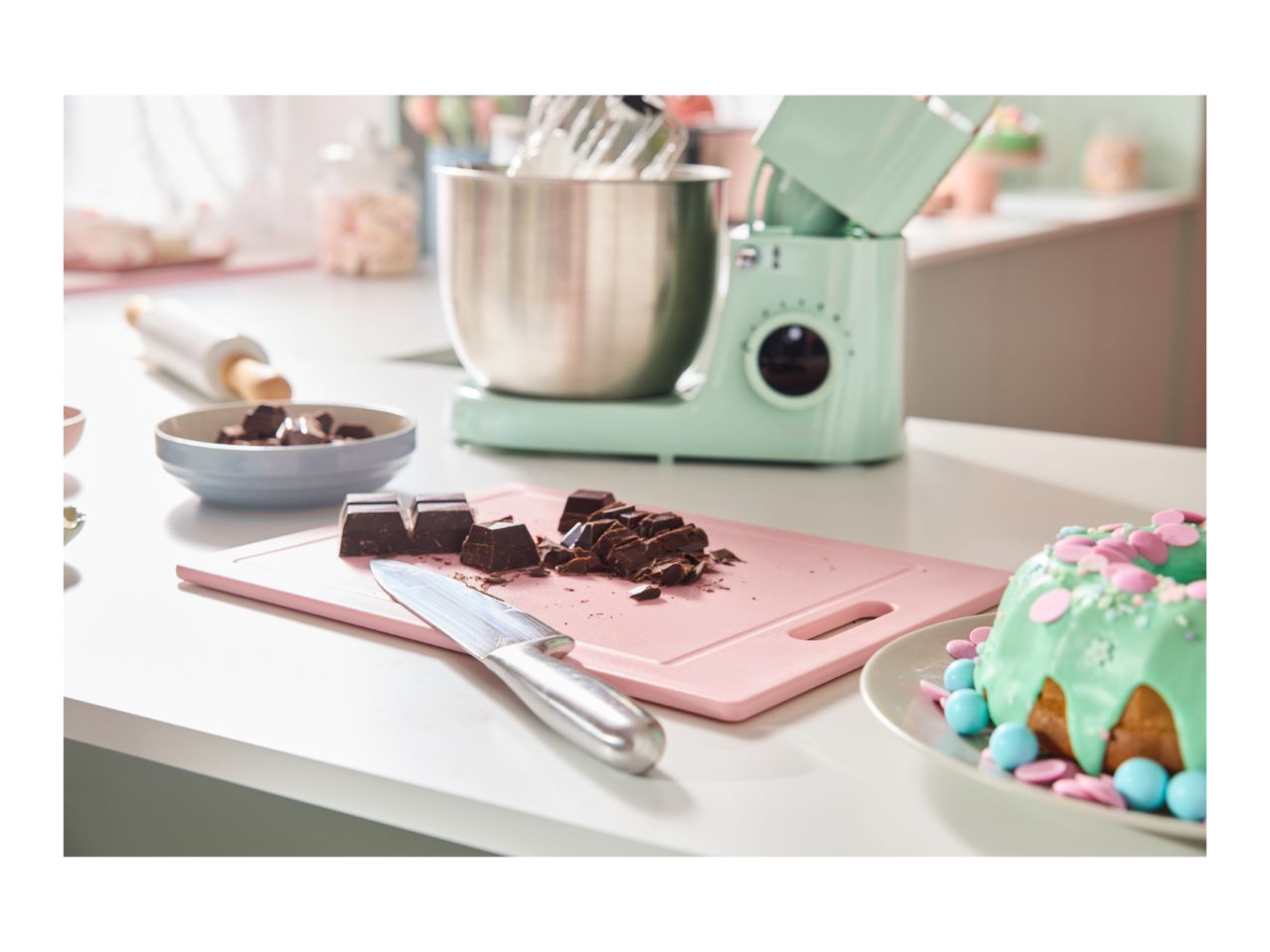 A kitchen counter with baking ingredients, a stand mixer, and a decorated cake.