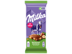 Une tablette de chocolat au lait aux noisettes entières, avec une vache et des montagnes en arrière-plan.