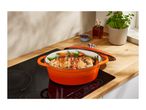 An orange Dutch oven with a roasted chicken and vegetables on an induction cooktop.