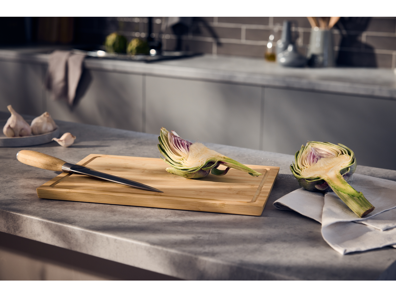 Artichoke halves and a knife on a cutting board in a kitchen setting.
