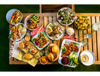 A vibrant summer picnic spread features grilled meats, salads, and sides on a wooden table.