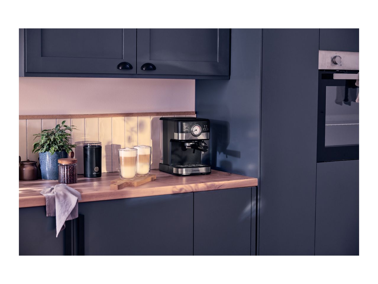 Espresso machine and two latte macchiato glasses on a wooden kitchen counter.