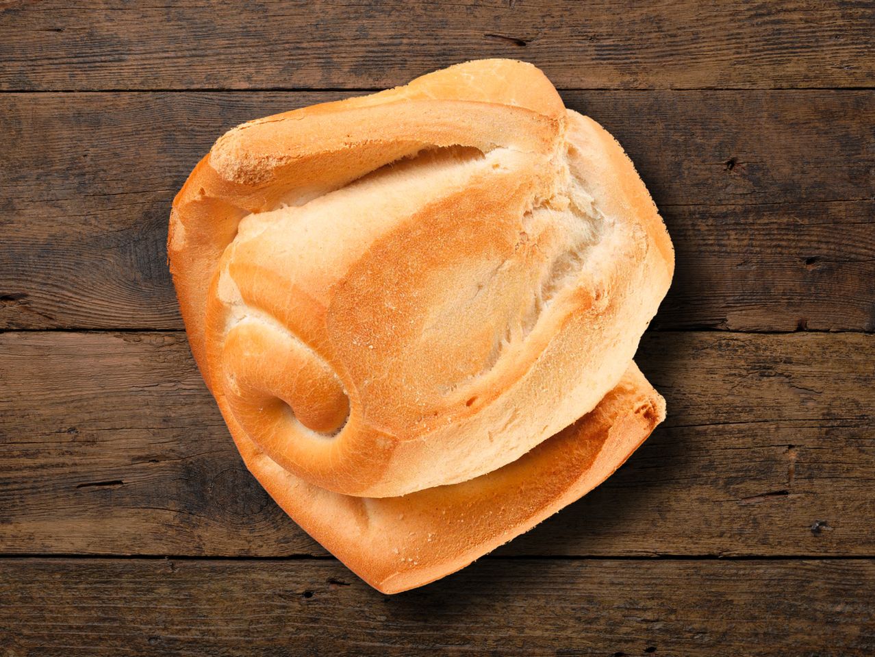 Ein goldbraunes, handwerklich gebackenes Brot liegt auf einem rustikalen Holztisch.