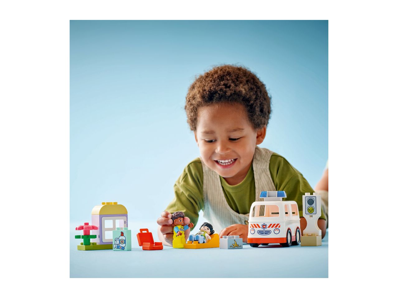 A child playing with an ambulance toy set, featuring figures and a small house.