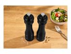 Black salt and pepper mills on a wooden table next to a bowl of salad and a fork.