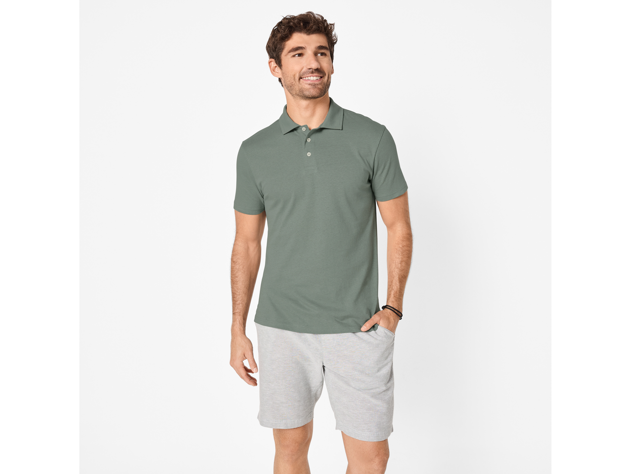 Bărbat purtând un tricou polo verde-gri și pantaloni scurți gri deschis, zâmbind și privind într-o parte.