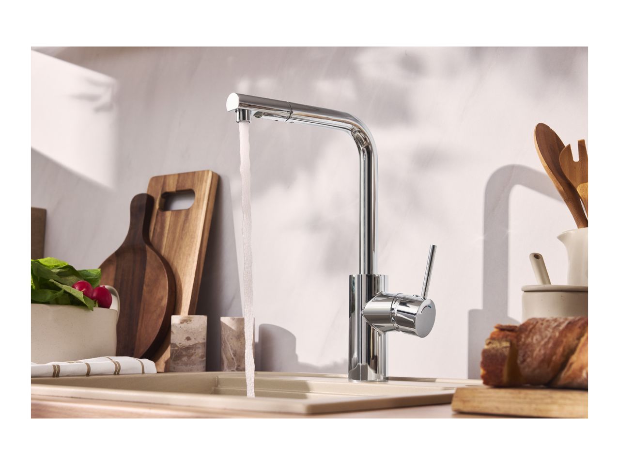 Chrome kitchen faucet with running water, sink, cutting boards, and fresh produce.