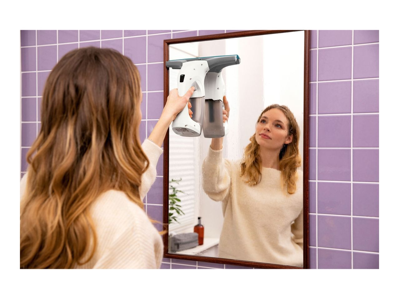 Woman cleaning a bathroom mirror with a window vacuum cleaner.
