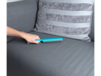 A hand holds a teal fabric brush, cleaning a gray couch.