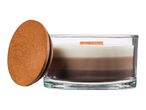 A layered candle in a clear glass container with a wooden lid, featuring white, light brown, and dark brown wax.