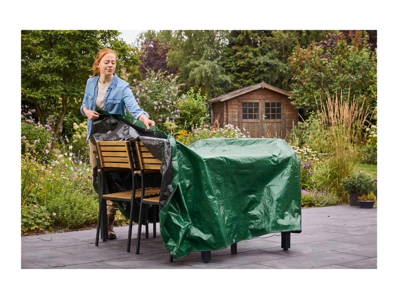 Woman covering outdoor furniture with a green protective tarp in a garden setting.
