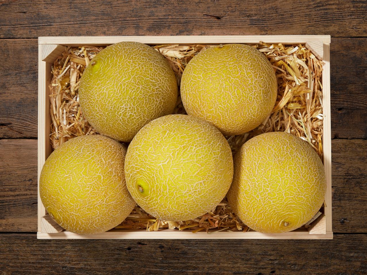 Vier Melonen in einer Holzkiste.