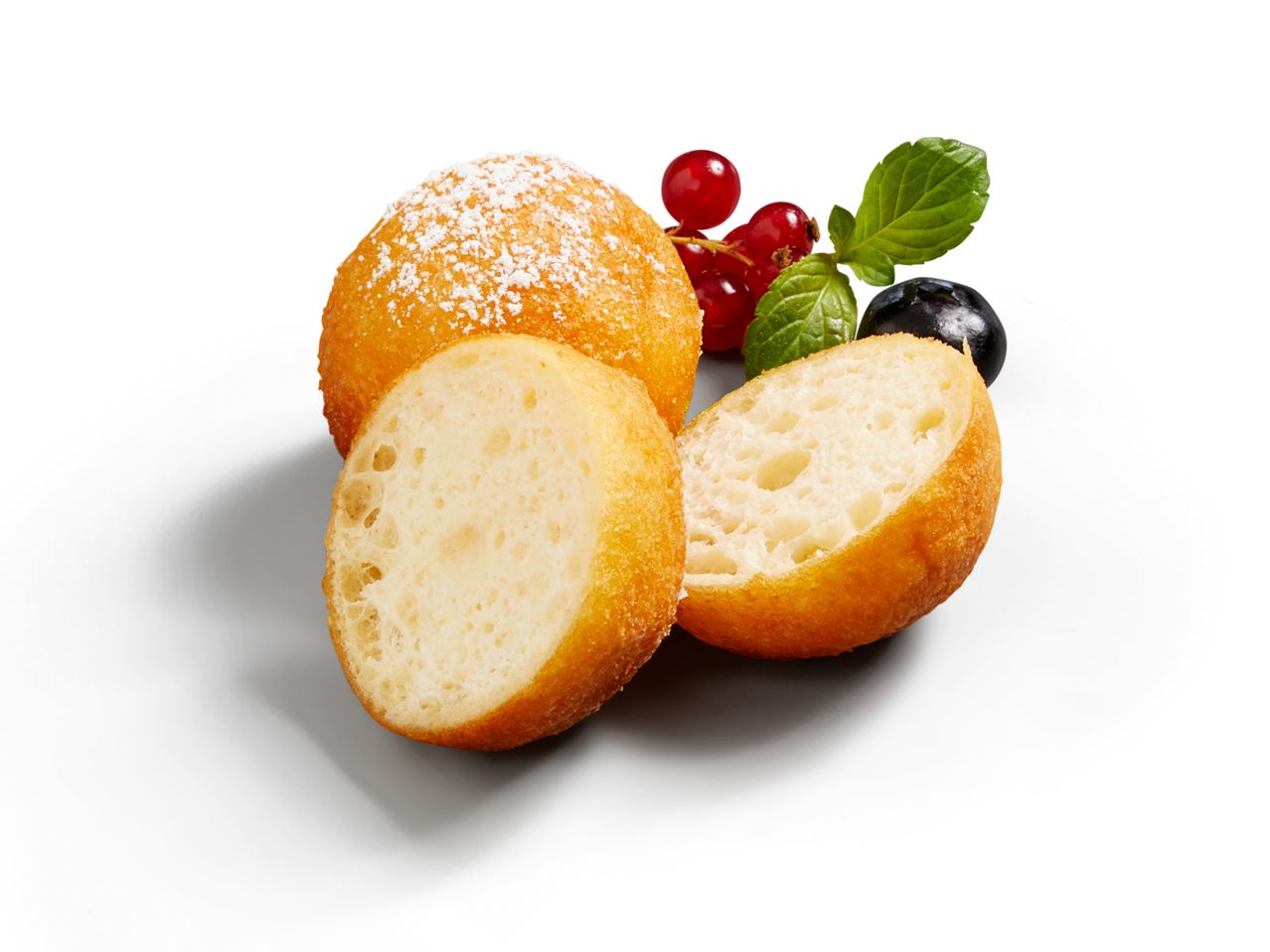 Zwei goldgelbe, mit Puderzucker bestäubte Krapfen, einer halbiert, neben roten Johannisbeeren und einem Minzblatt.