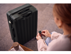 Woman holding keys and a tracker, next to her a black Esmara suitcase and a coffee cup.