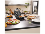 Gaufrier ouvert avec un sandwich grillé, entouré d'ingrédients frais sur un comptoir de cuisine.