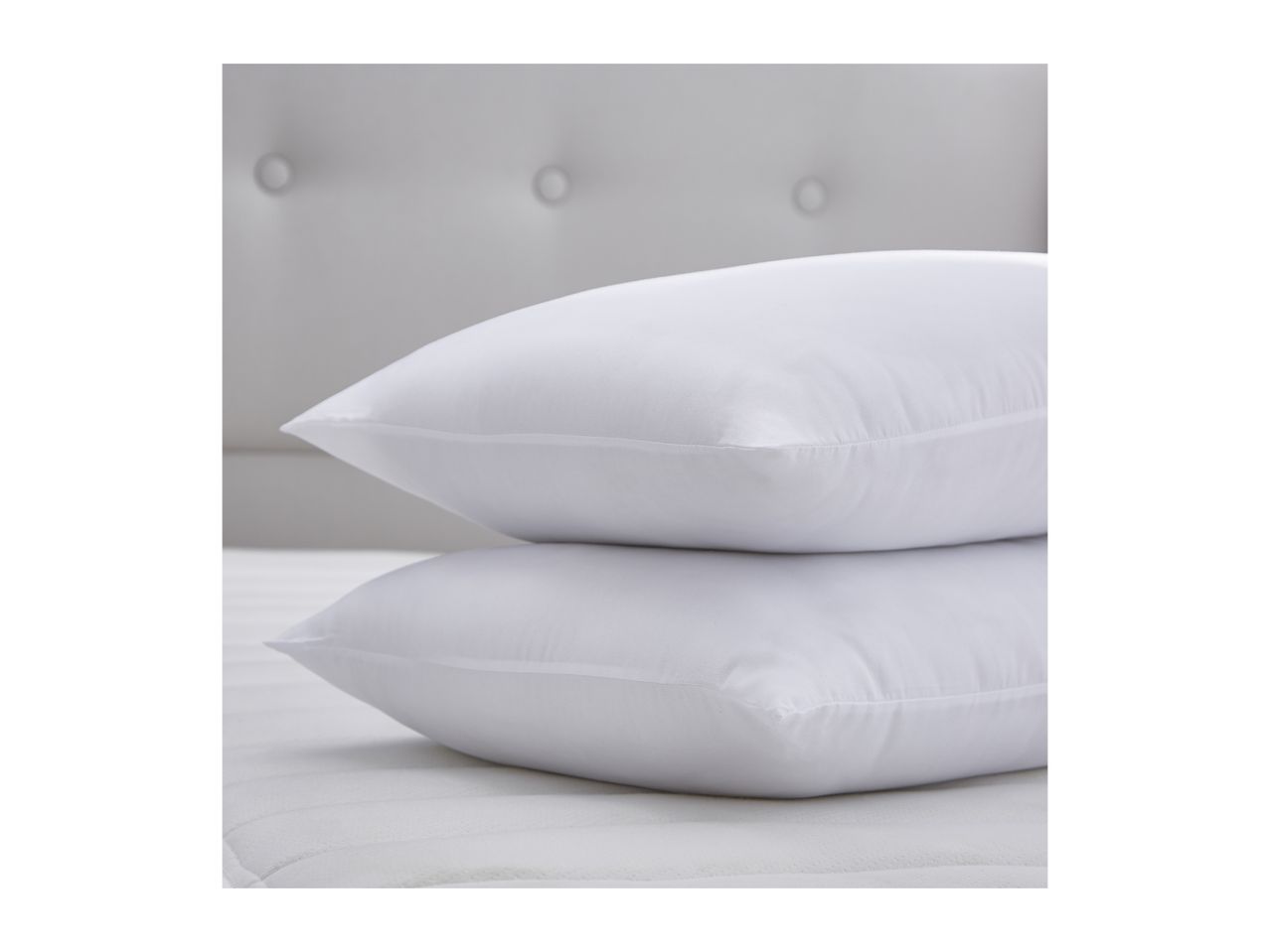 Two white pillows stacked on a mattress with a tufted headboard in the background.